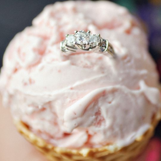 Pale
                      pink ice cream in a waffle cone. A three diamond
                      engagement ring sits on top of the ice cream.