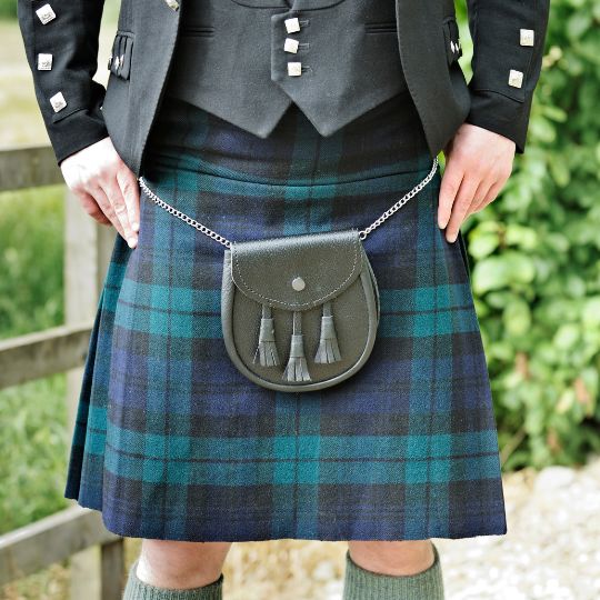 Man
                      standing with his legs slightly apart and his
                      hands on his hips. He is wearing a kilt, and a
                      Prince Charlie jacket and waistcoat